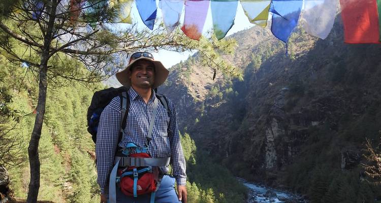 Lächelnder Wanderer mit Gebetsfahnen und malerischer Berglandschaft.
