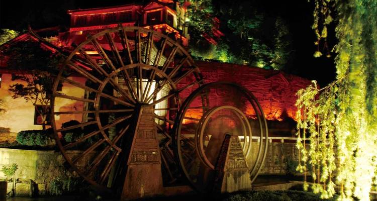 Grandes ruedas de agua iluminadas y edificios antiguos por la noche.
