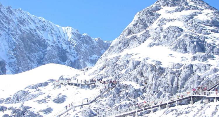 Montaña cubierta de nieve con visitantes subiendo por una pasarela.