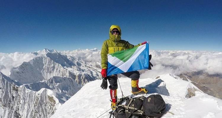 Bergbeklimmer op een besneeuwde top die een vlag vasthoudt.
