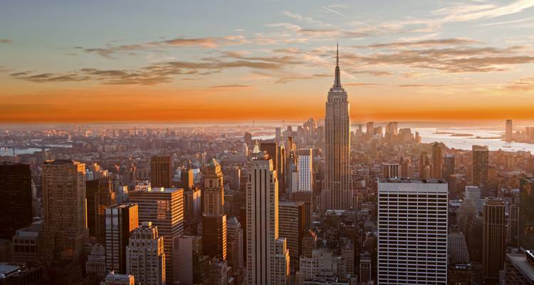 Le skyline de New York City brillant d'une lumière orange chaleureuse au coucher du soleil, mettant en évidence l'Empire State Building sur un horizon urbain expansif.
