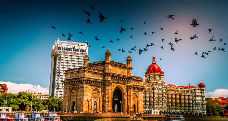Puerta de la India y Hotel Taj Mahal Palace bajo un cielo azul vívido con pájaros en vuelo.