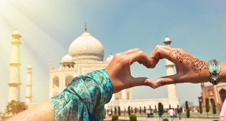 Dos manos adornadas con henna forman un corazón enmarcando el Taj Mahal de mármol blanco.