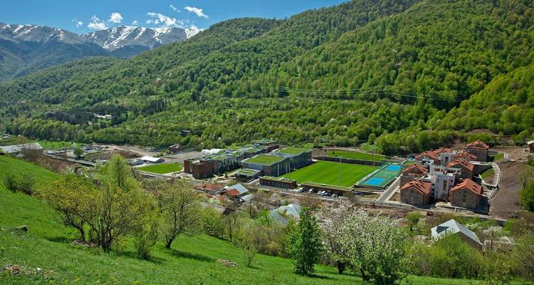 A lush green valley surrounded by mountains with small buildings.