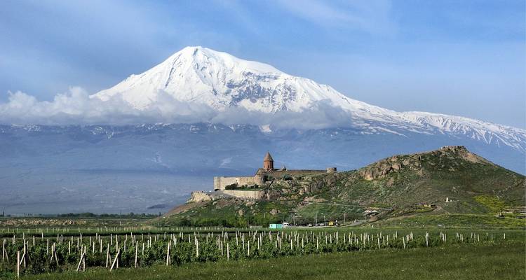Monastery on a hill with snowy mountain backdrop.