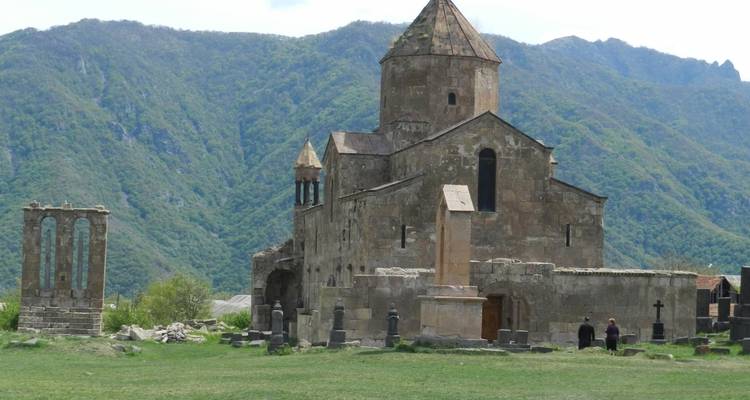 Old stone church with mountains and people nearby.