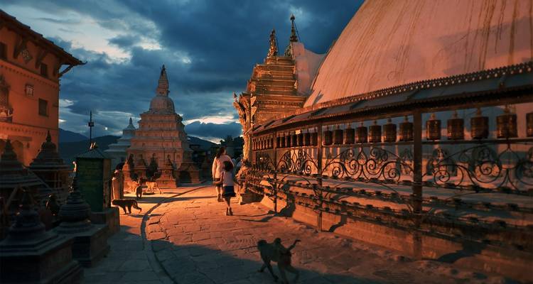 Stupa en gebedsmolens in de schemering met een wandelende persoon.