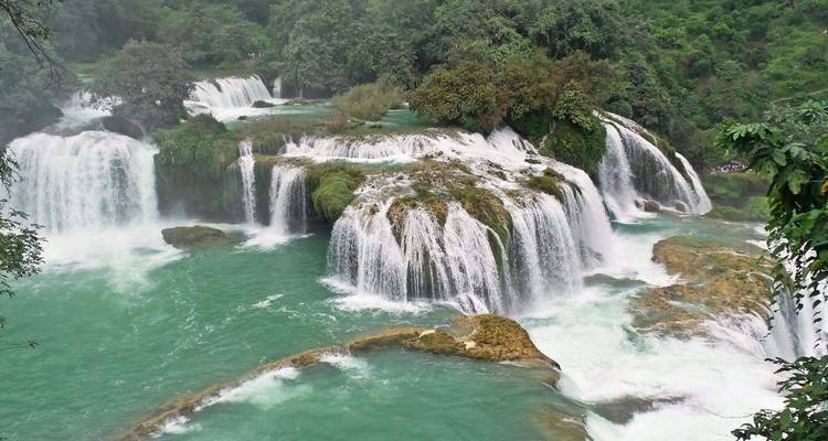 Wasserfälle, die in ein türkises Becken stürzen, umgeben von Grün.