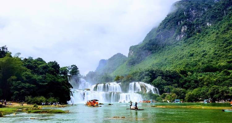 Cascada fluyendo hacia un río rodeado de exuberantes paisajes verdes.