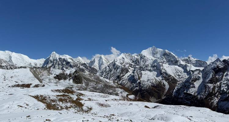 Panoramisch uitzicht op sneeuwbedekte Himalaya-toppen onder een diepblauwe hemel.
