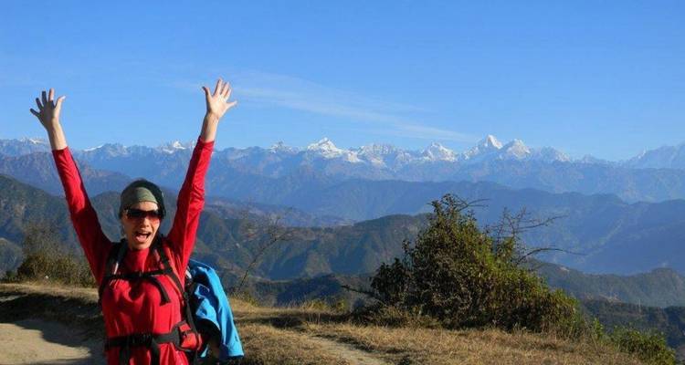 Excited person with raised arms in front of mountain range.