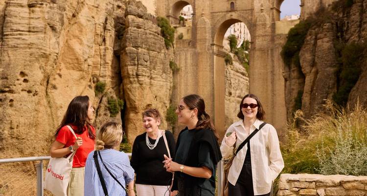 Travelers chatting with the Puente Nuevo bridge and deep gorge of Ronda behind them