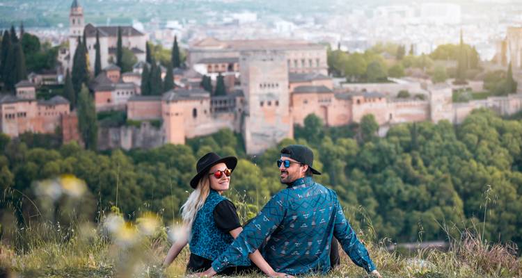 Ein Paar entspannt sich auf einem grasbewachsenen Hügel mit Blick auf die Alhambra und die Stadt Granada unter sanftem Nachmittagslicht.