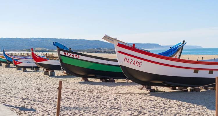 Des bateaux de pêche colorés avec 'Nazaré' écrit sur les côtés sur une plage de sable.