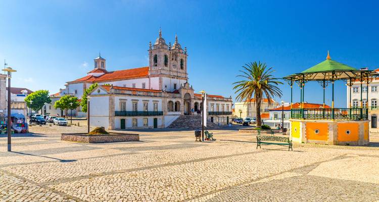 Place de ville ensoleillée avec architecture historique et un palmier.