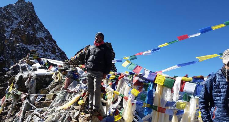 Personne debout parmi des drapeaux de prière colorés sur une colline rocheuse avec des montagnes.