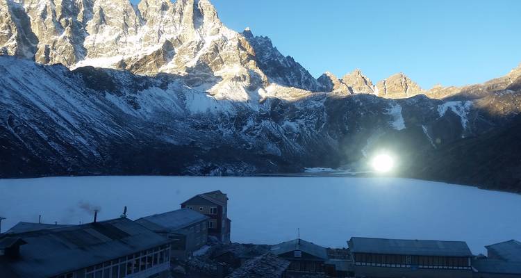 Lac gelé avec des montagnes enneigées en arrière-plan, des bâtiments à proximité.