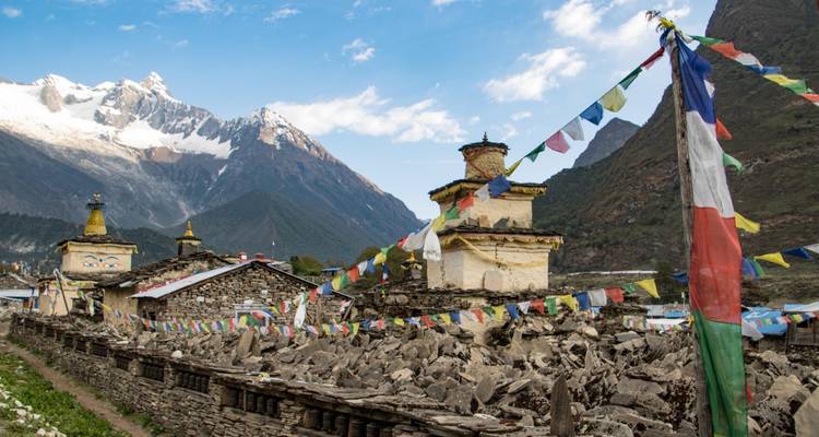 Bergdorf mit Gebetsfahnen und schneebedeckten Gipfeln.