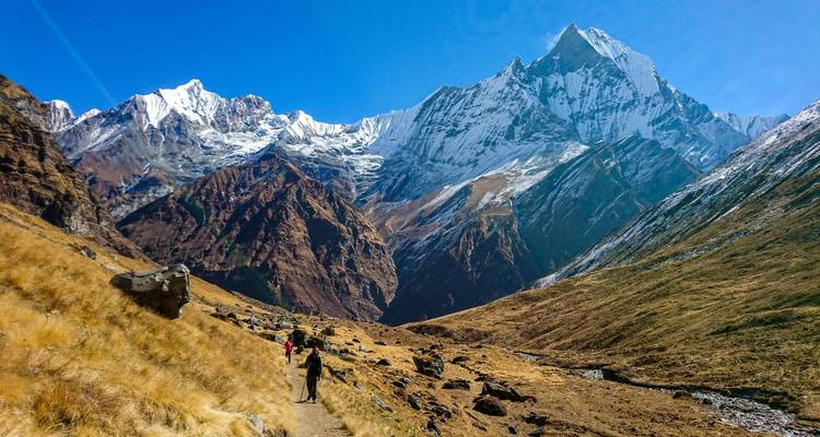Wanderer, der einen Pfad entlanggeht mit schneebedeckten Bergen in der Ferne.