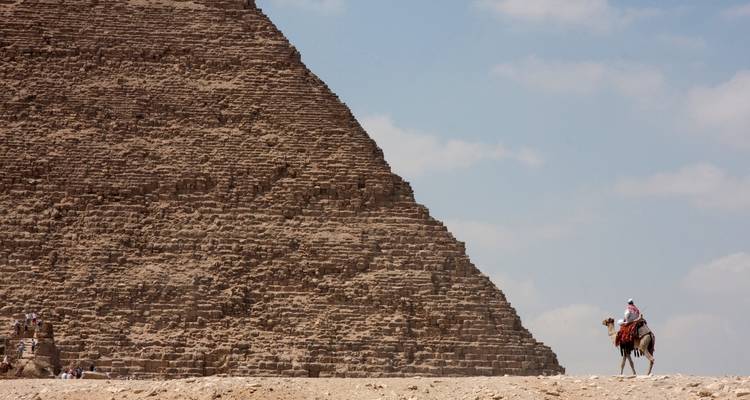 Eine große Pyramide mit einer Person, die im Vordergrund auf einem Kamel reitet.