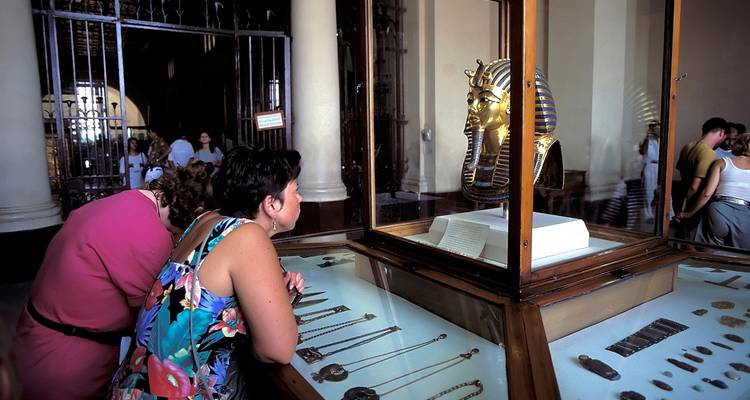 Besucher, die eine goldene Grabmaske in einer Museumsausstellung betrachten.