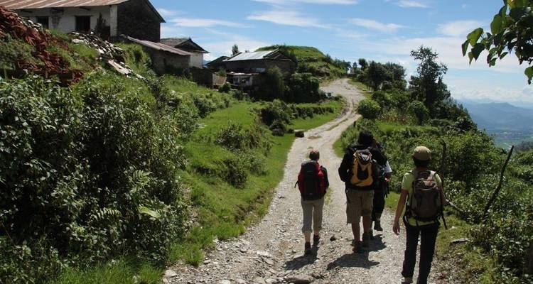 Hikers walking on a dirt road beside a hillside village.