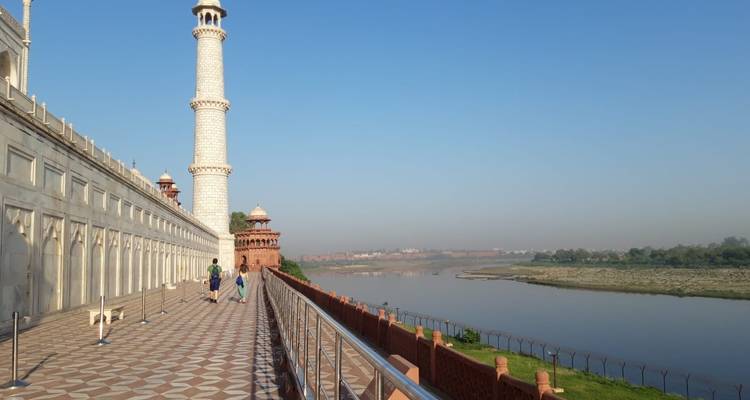 Vista lateral del Taj Mahal con visitantes distantes y río.