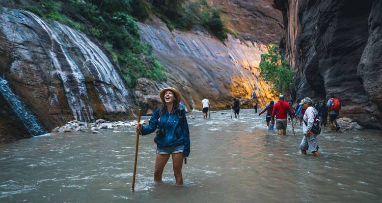 Los aventureros vadean a través de la garganta del río Narrows con bastones de caminar entre imponentes paredes de cañón.