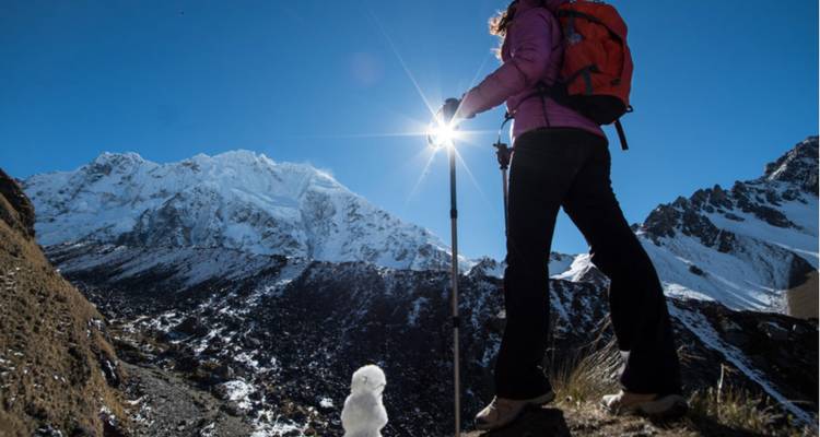 Un excursionista permanece de pie mirando hacia montañas nevadas con un cielo azul brillante.