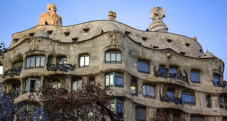 La fachada ondulante de piedra de la Casa Milà de Gaudí captura la cálida luz del atardecer contra un cielo azul.