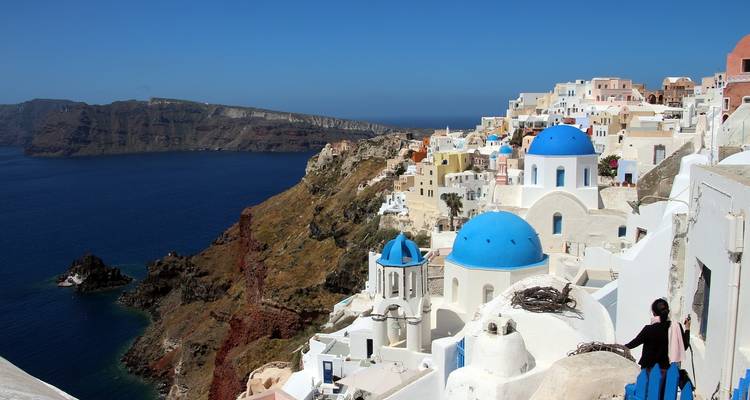 Vista panorámica de la caldera de Santorini con iglesias de cúpulas azules y casas blancas en cascada por el acantilado.