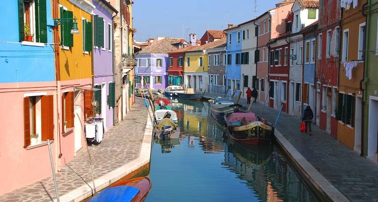 Narrow canal flanked by vividly painted houses and moored boats on Burano island.