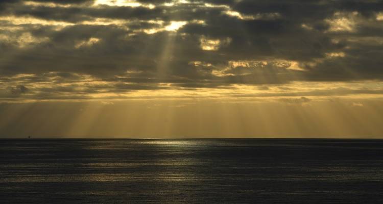 Sunbeams streaming through clouds over the ocean.