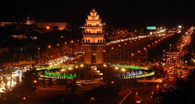 Een nachtelijk zicht op een monument omringd door verkeer en kleurrijke lichten.
