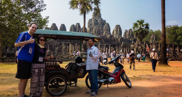 Turistas con un guía y una motocicleta frente a las ruinas de un templo antiguo.