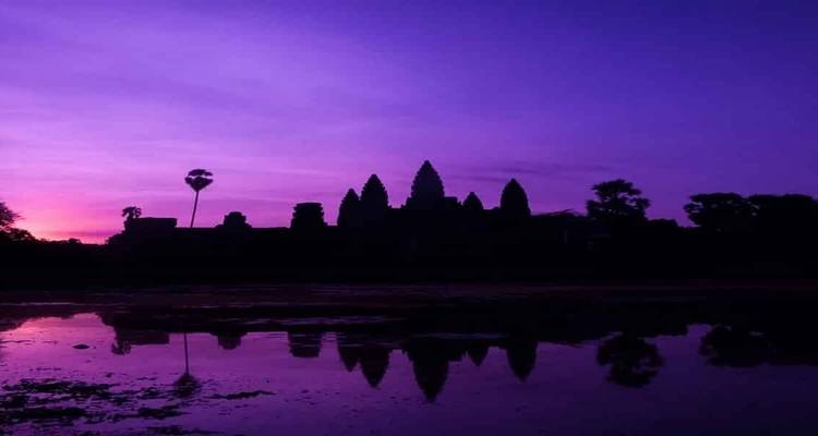 Silhouet van Angkor Wat tijdens een levendige paarse zonsopgang boven een waterreflectie.