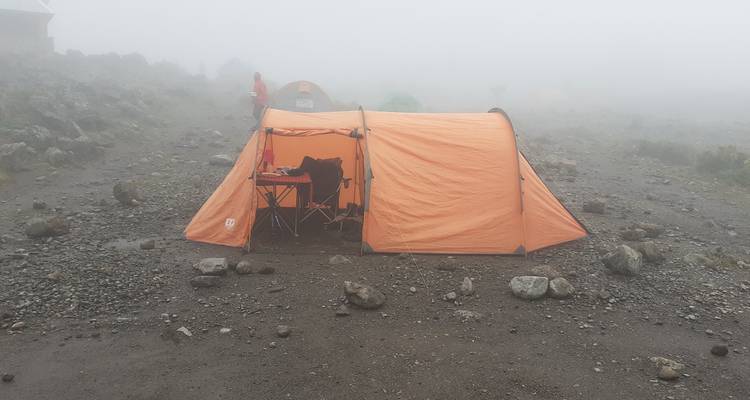 Oranges Zelt auf einem nebligen Bergcampingplatz mit steinigem Boden.
