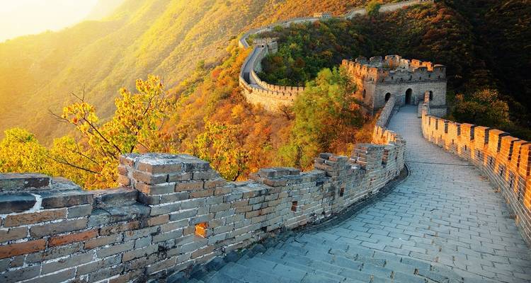 Grote Muur van China die zich uitstrekt over een bergachtig landschap bij zonsondergang.