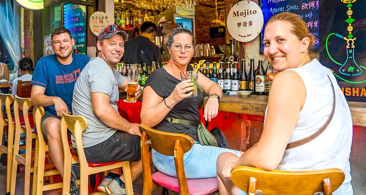 Cuatro amigos se relajan en taburetes de bar, disfrutando de bebidas dentro de un pub colorido e iluminado con neón.