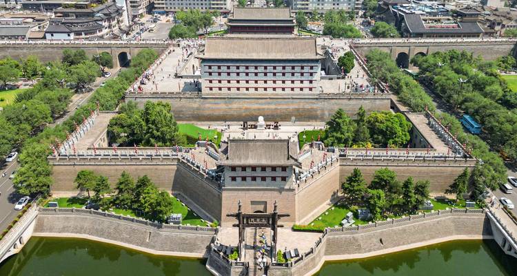 Vista aérea con dron de las imponentes murallas antiguas y puertas de la ciudad de Xi'an rodeadas de jardines verdes y un foso.