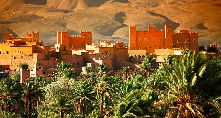 Les oasis de palmiers et les kasbahs en terre cuite se dressent devant les pentes montagneuses arides à la lumière chaude du soir.
