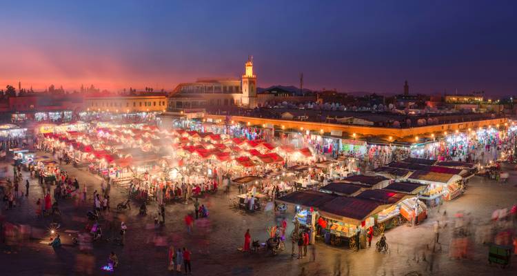 Vue panoramique nocturne des étals de nourriture remplis de fumée et des foules colorées dans la place principale de Marrakech.