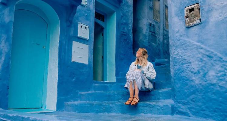 Junge Frau, die auf blauen Stufen sitzt, umgeben von lebendigen indigoblauen Wänden und Türen in einer historischen Stadt.