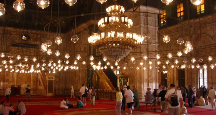 Interior de una mezquita con candelabros encendidos y gente.