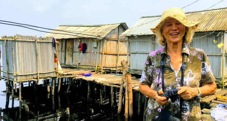 Mujer sonriendo en un pueblo pesquero con casas sobre pilotes.