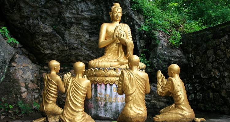 Estatuas doradas de Buda con monjes rezando.