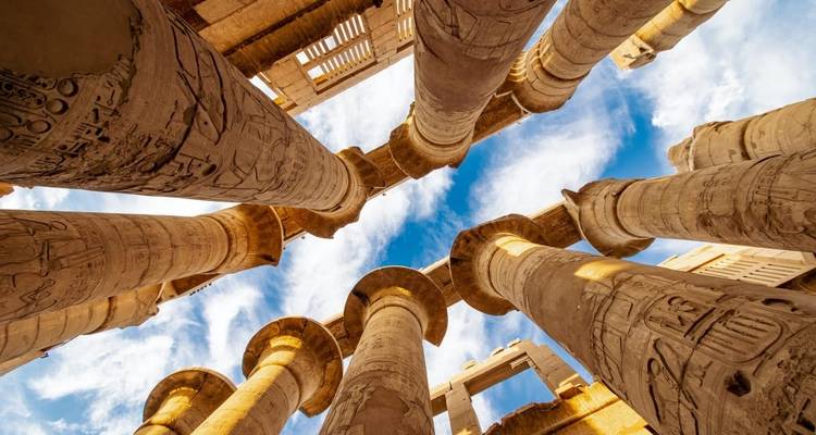 Columnas antiguas con jeroglíficos que se alzan hacia un cielo azul.