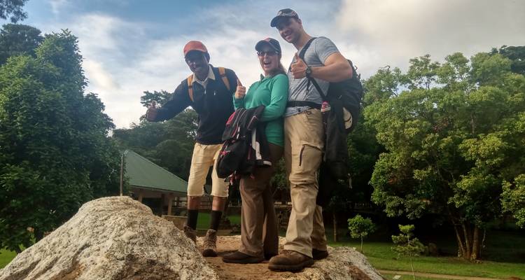 Drei Wanderer auf einem großen Felsen in einer Parklandschaft.