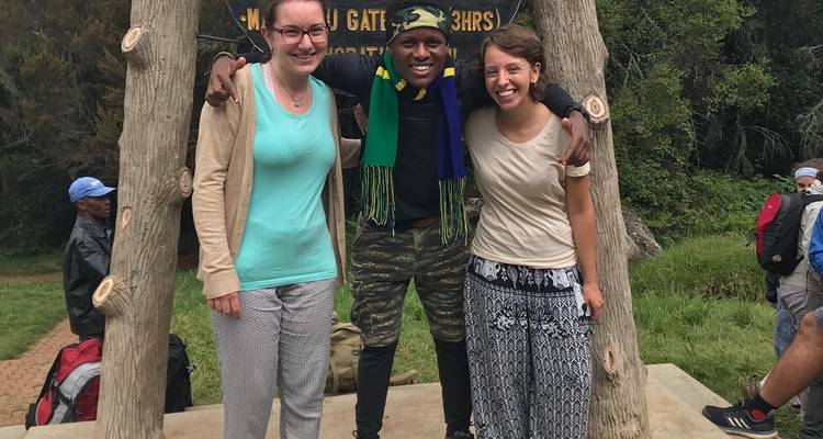 Drei Personen stehen unter einem hölzernen Torbogen mit einem Naturpfad im Hintergrund.