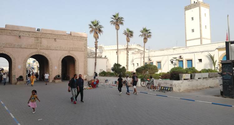 Personas caminando frente a una puerta arqueada y edificios históricos.